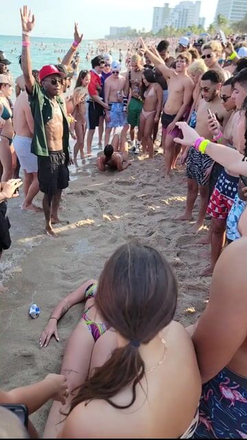 Beach party crowd in swimwear; dancing in crowd context, no close-ups