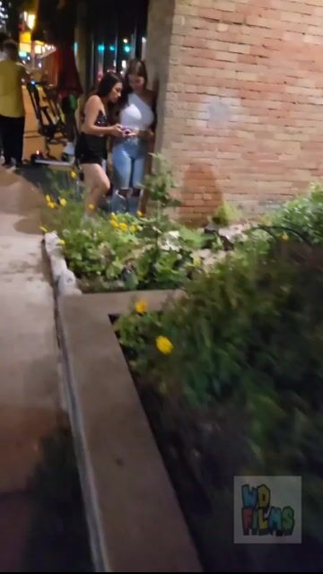 Two women by brick wall at night, fully clothed